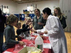 Teacher in lab coat leads students, parents in chemistry experiment