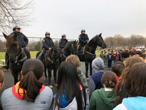 Four mounted police officers face a crowd of students for outdoor lesson