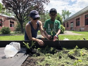 Mentor Sabina Tyler handing student a plant in garden bed