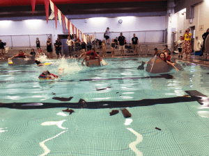 Students paddling across pool in cardboard boats