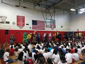 Teachers in cartoon-like costumes in gym with crowd of students
