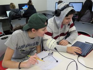 Students sitting at desk in front of computer and microphone.